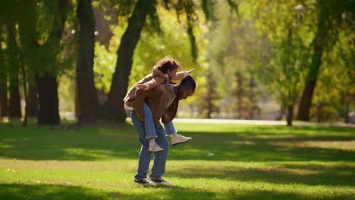 Playful Father Piggybacking Daughter Enjoying Family Weekend in Sunny Park