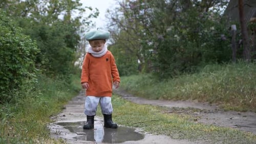 Spring Break, Cute Male Child in Hat and Rubber Boots Have Fun Jumping in Dirty Puddle