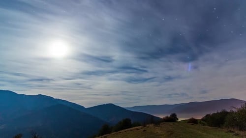 Night Sky with Clouds and Moon Over Mountains