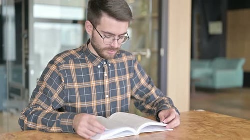 Hardworking Young Designer Reading Book in Office