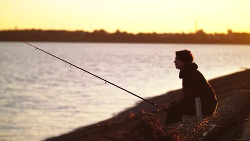 Der Fischer fängt Fische. Schießen im Profil. Fischer vor dem Hintergrund von Wasser und Orange