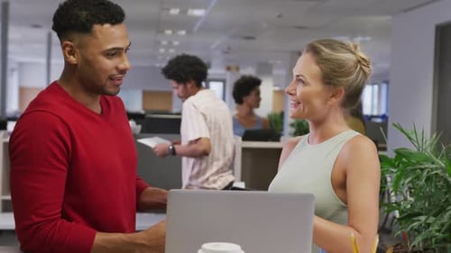 Happy diverse male and female business colleagues talking and using laptop