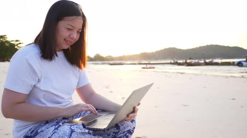 Freelancer Asian woman using laptop online working on the beach