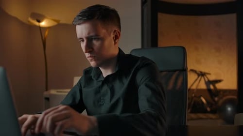A Young Man Works on a Laptop Typing on a Keyboard