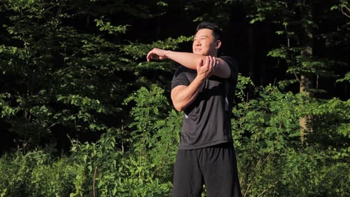 Strong Asian Runner Stretching Arms Before Exercising in Summer Park at Sunset