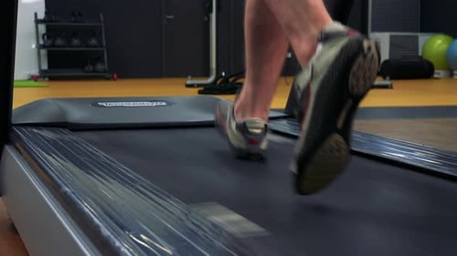 Ein fitter Mann joggt auf einem Laufband in einem Fitnessstudio - Nahaufnahme an den Füßen von hinten
