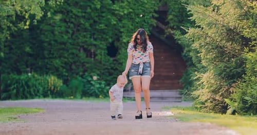 Happy Mother with Her Little Son Go Along the Path in the Park