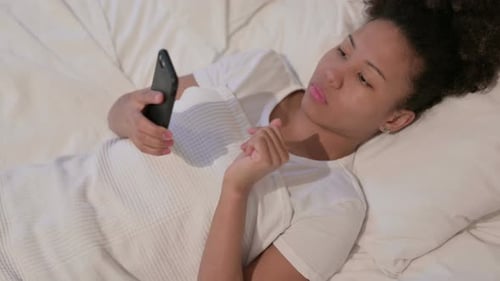 Young Woman Lying In Bed Using Mobile Phone