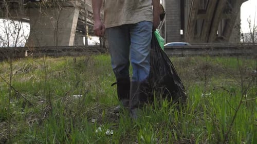 Adult Carrying Trash Bag Through Grassy Urban Area