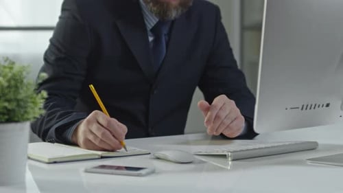 Businessman at Computer Taking Notes in Modern Office