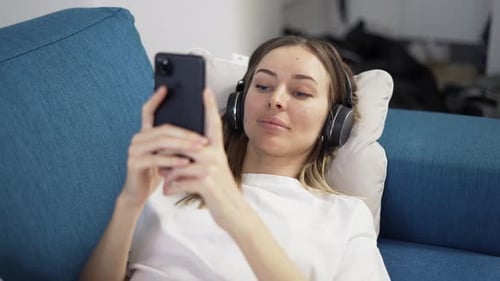 Woman Relaxing on Couch Using Smartphone with Headphones