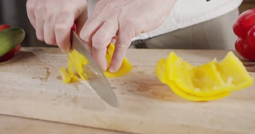Slow motion close up of a chef knife slicing a yellow bell pepper