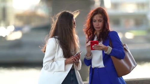 Two Cheerful Ladies Are Using Smartphones on Street in City, Colleagues and Friends