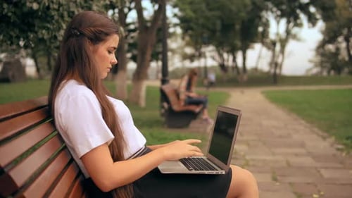 Woman Using Laptop on Bench in Park