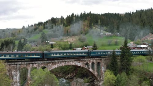 Passenger train passing over viaduct bridge in mountains landscape.