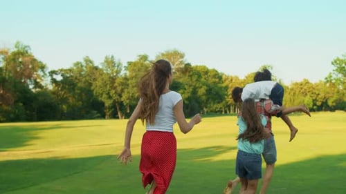 Family Running in Field. Happy Children and Parents Playing with Ball in Meadow