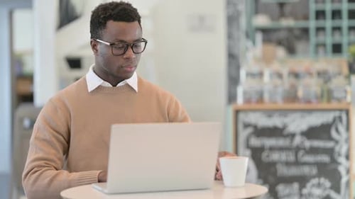 Creative African Man Drinking Coffee While Using Laptop in Cafe