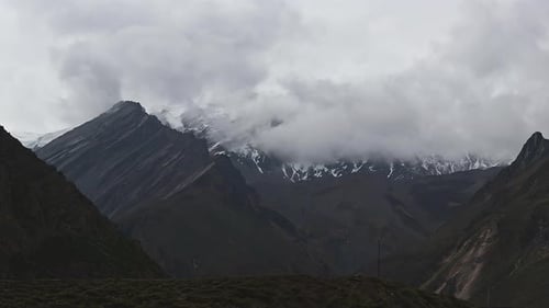 Timelapse Clouds Swirl Over a Mountain Valley a Snowy Peak in the Distance