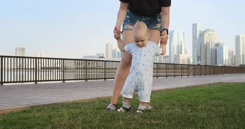 Smiling Boy Holding His Mother's Hand Makes the First Steps Walking Along the Promenade in the