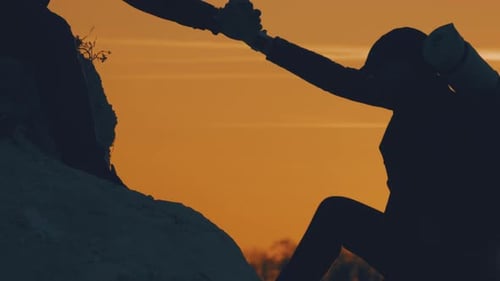 Silhouette of Helping Hand Between Two Climber. Two Hikers on Top of the Mountain, a Man Helps a