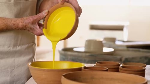 Partie centrale d'une potière versant de la peinture dans un bol