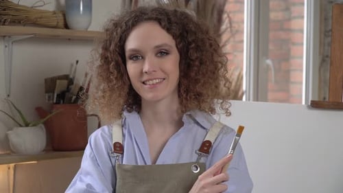Young Adult Woman Smiling and Holding Paintbrush in Studio