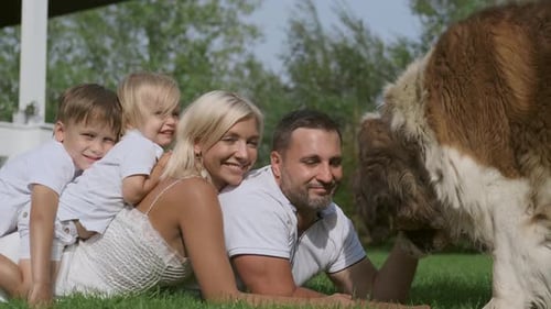 Smiling Family Lying with Large Dog in the Grass