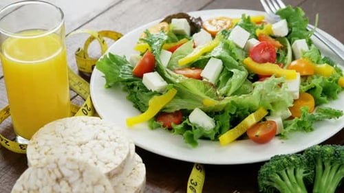 Vegetable salad with glass of juice, granola bar and measurement tape