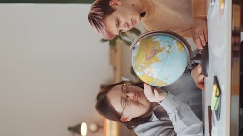 Two People Studying the Globe Together Indoors