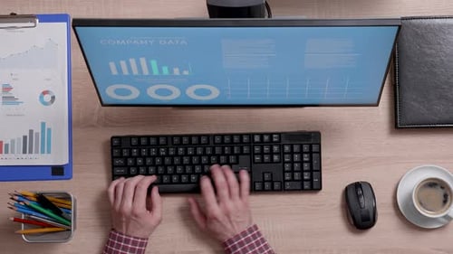 Draufsicht eines Mannes, der an seinem Computer arbeitet, mit Daten von Finanzunternehmen auf seinem Monitor