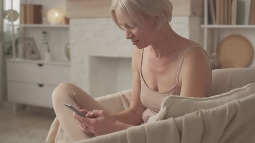 Woman Relaxing in Chair Using Smartphone at Home
