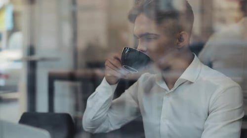 Young Businessman Using Laptop Computer at Cozy Coffee Shop and Drinking Coffee