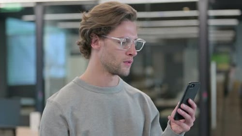 Man Celebrates Success on Smartphone in Modern Office
