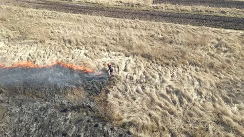Aerial View of Firemen Extinguishing Grassland Field Burning with Red Fire During Dry Season