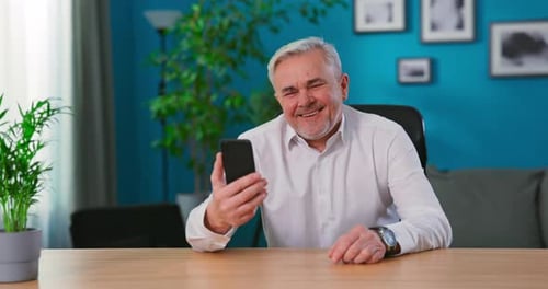 Smiling Senior Man Using Smartphone at Desk