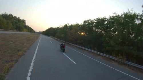 Biker Is Accelerating at Motorcycle on Empty Country Road. Man Riding Fast on Modern Sport Motorbike