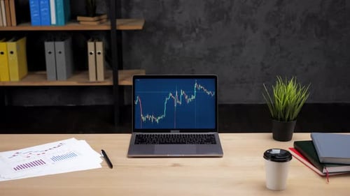 Laptop Computer with Chart of Stock Exchange on Screen Stands on Table in Office
