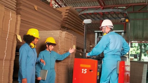 Workers team inspect stock at factory warehouse, management piles of cardboard.