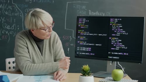 Programmierschullehrer erklärt Softwarecodierung, zeigt auf Computerbildschirm und spricht