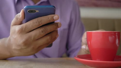 Close Up of Young Man Hand Using Smart Phone and Drinking Coffee at Cafe