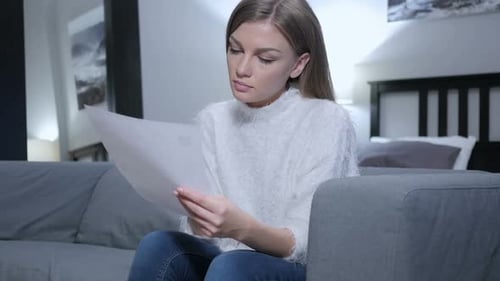 Woman Reading Document on Couch Indoors