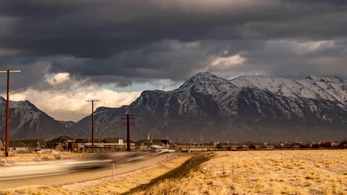Dramatisch Wolken ziehen an den schneebedeckten Bergen vorbei, während der Berufsverkehr entlang der Autobahn zoomt