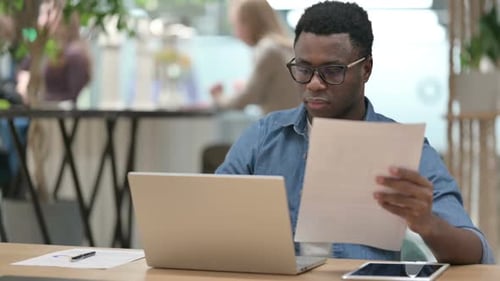 Adult reads papers while working on laptop