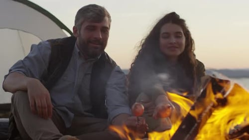 Male and Female Tourists Cooking Sausages over Campfire
