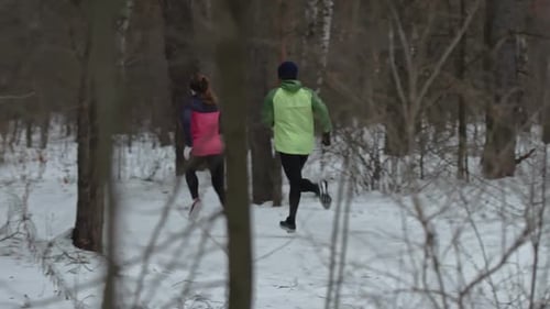 Two People Running Through Snow Covered Forest