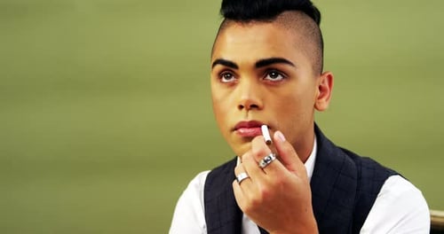 Androgynous man posing with cigarette against green background