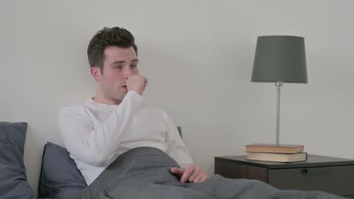Young Man Coughing while Resting in Bed