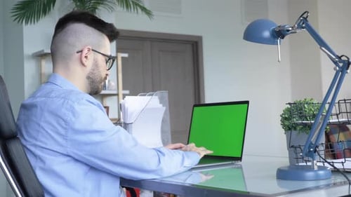 Young caucasian Man using a Laptop Green screen on the desk at home.
