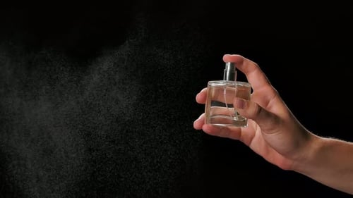 Hand Sprays Perfume Bottle Against Black Backdrop