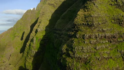 Grassy Mountain Slope Illuminated with Bright Sun Light, and Ocean Coastline Behind. Aerial Shot
